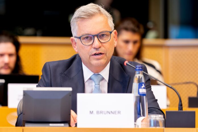 Magnus Brunner speaking into a microphone at a meeting table in the European Parliament