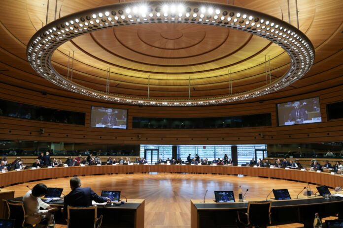Ministers seated around the circular table of the Council of the EU in Luxembourg during the Justice and Home Affairs Council, with a large ring of lights above