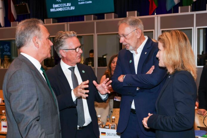 Four ministers stand in conversation beside the meeting table at Dublin Castle, under a screen with the Irish presidency’s ÉIRE2026.EU branding.