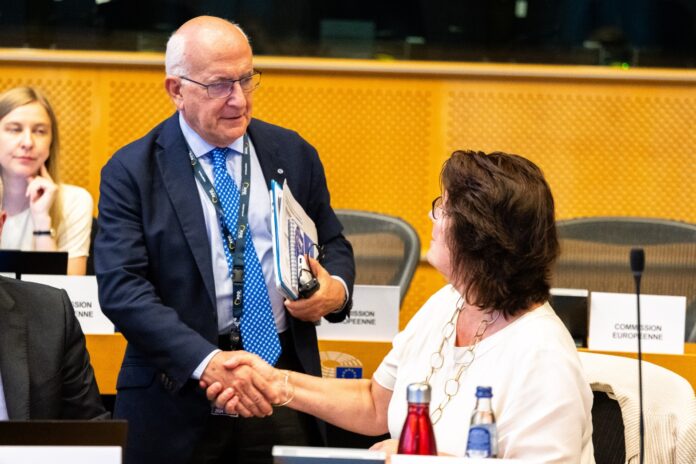 Javier Zarzalejos shakes hands with Beate Gminder across the negotiating table at the European Parliament, with European Commission name cards in front of her.
